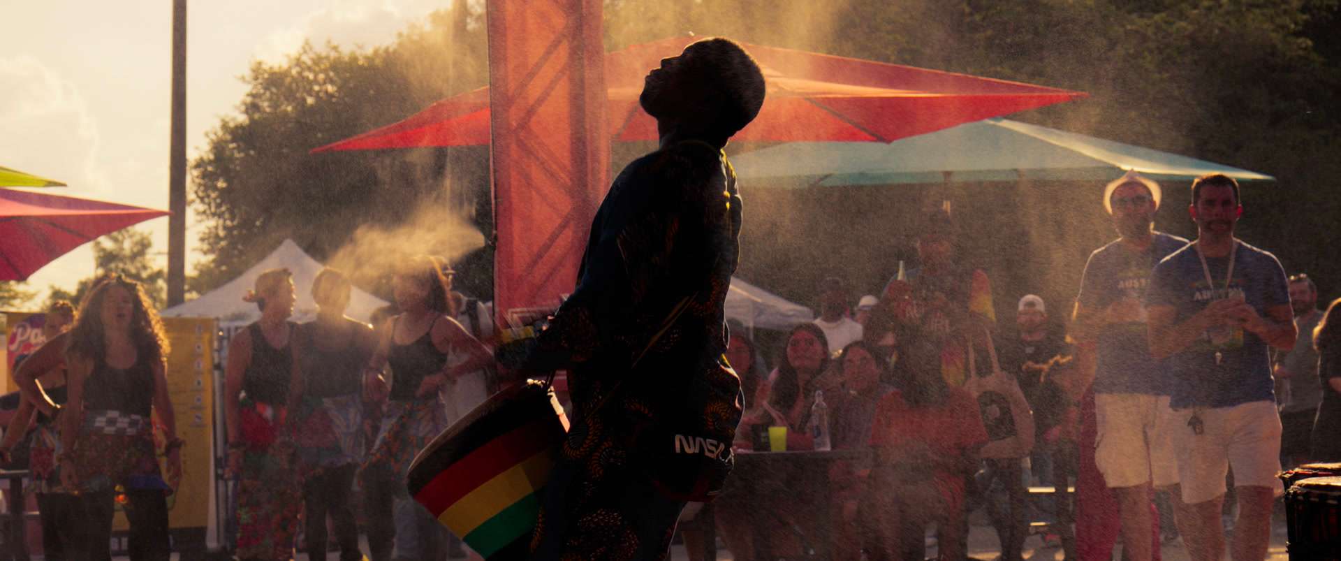 A drummer in silhouette, backlit by low sun through drifting mist at an Austin street festival.